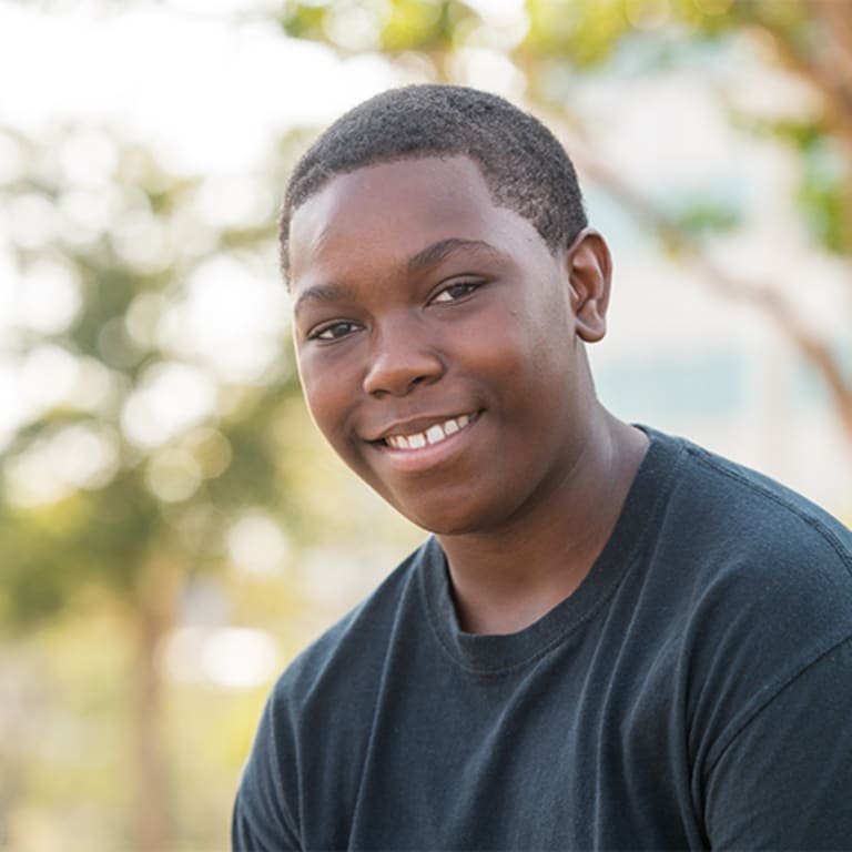 smiling teenage boy sitting in front of a tree outside