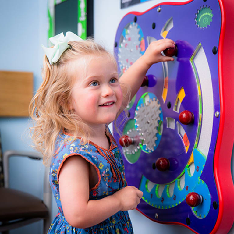 small smiling girl playing with a puzzle on the wall in a hospital room
