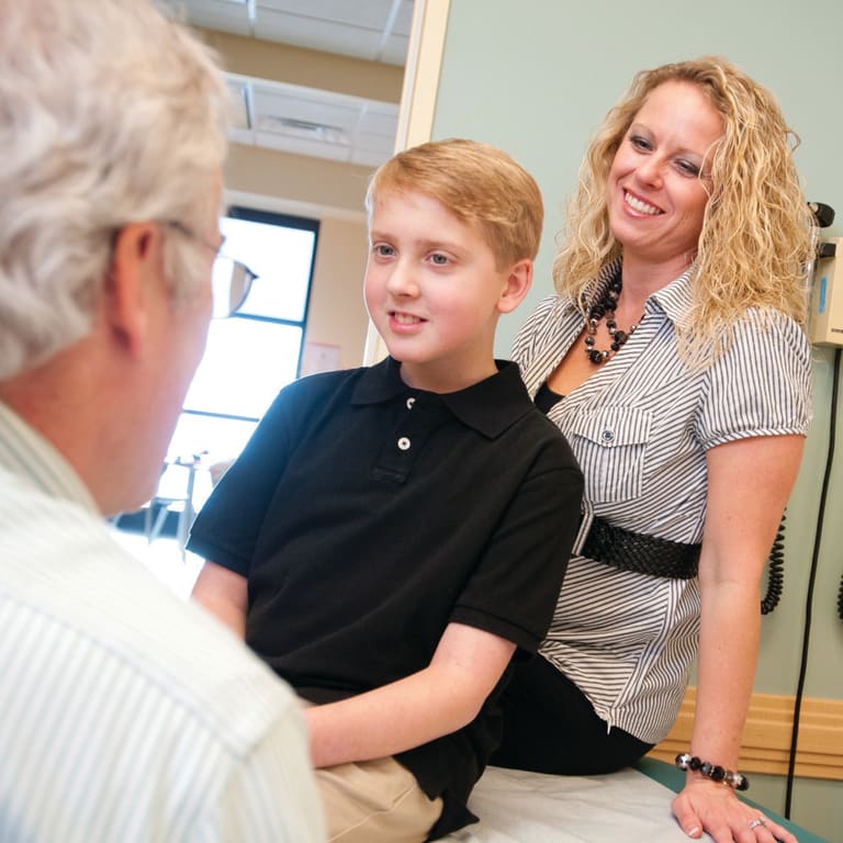 doctor talks with an older elementary age boy and his mom in an exam room