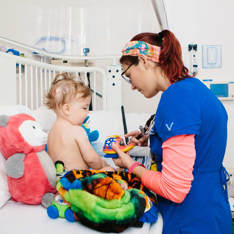 nurse sharing a small toy helicopter with an infant in a hospital bed