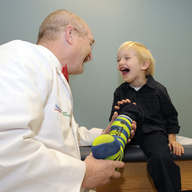 small boy in leg cast laughing with his doctor