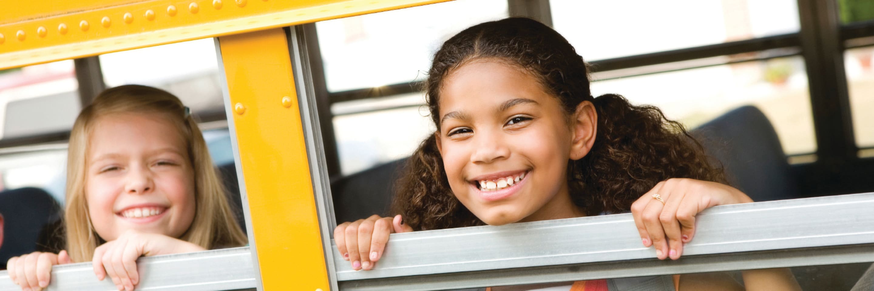 two girls smiling and looking through a school bus window