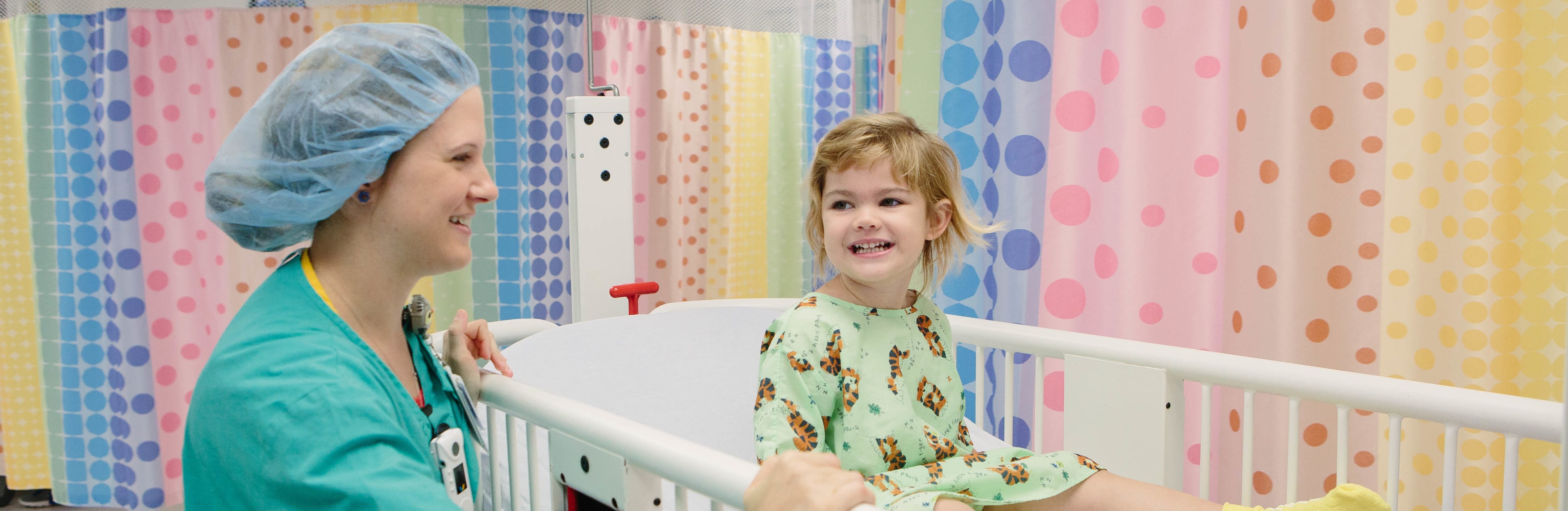 a happy little girl is wheeled into surgery by a smiling, caring nurse.