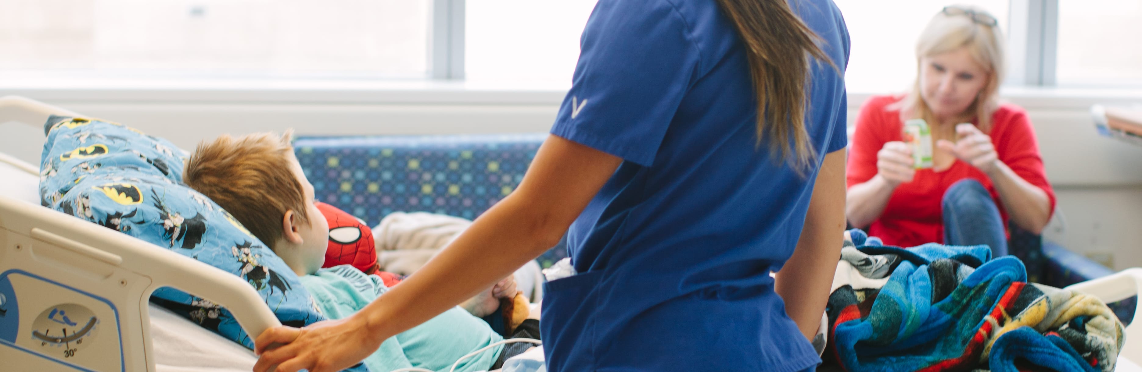A child in a hospital bed with a nurse standing next to it while mom looks on