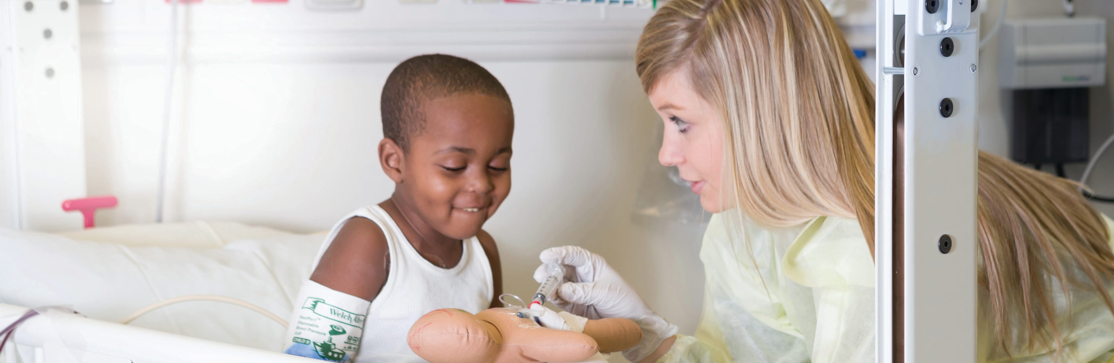female child life specialist shows a young boy how a blood draw works using a doll
