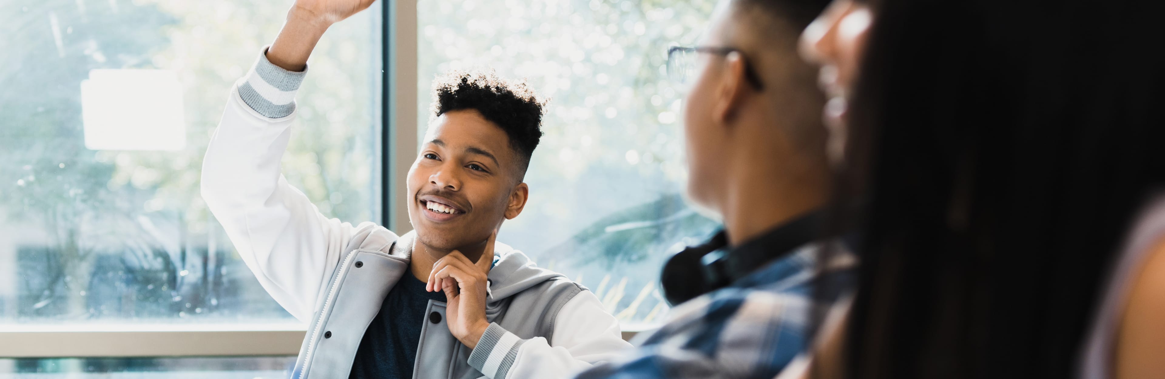 Teenage boy with a cool attitude raises his hand and smiles as he entertains 2 other classmates