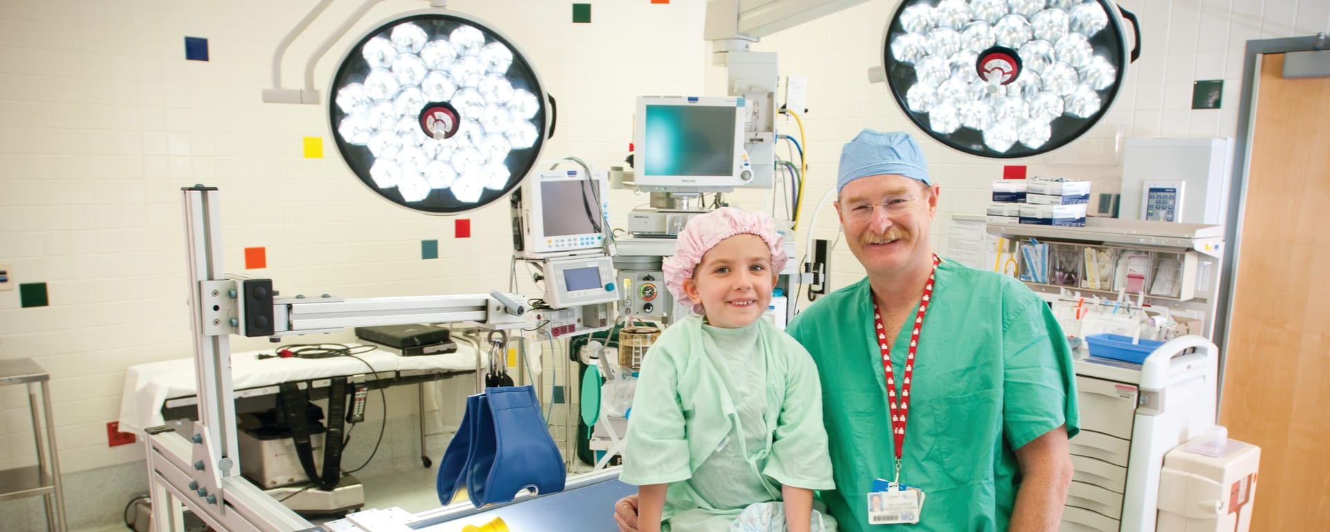 smiling male doctor standing next to a young female patient sitting on an operating table