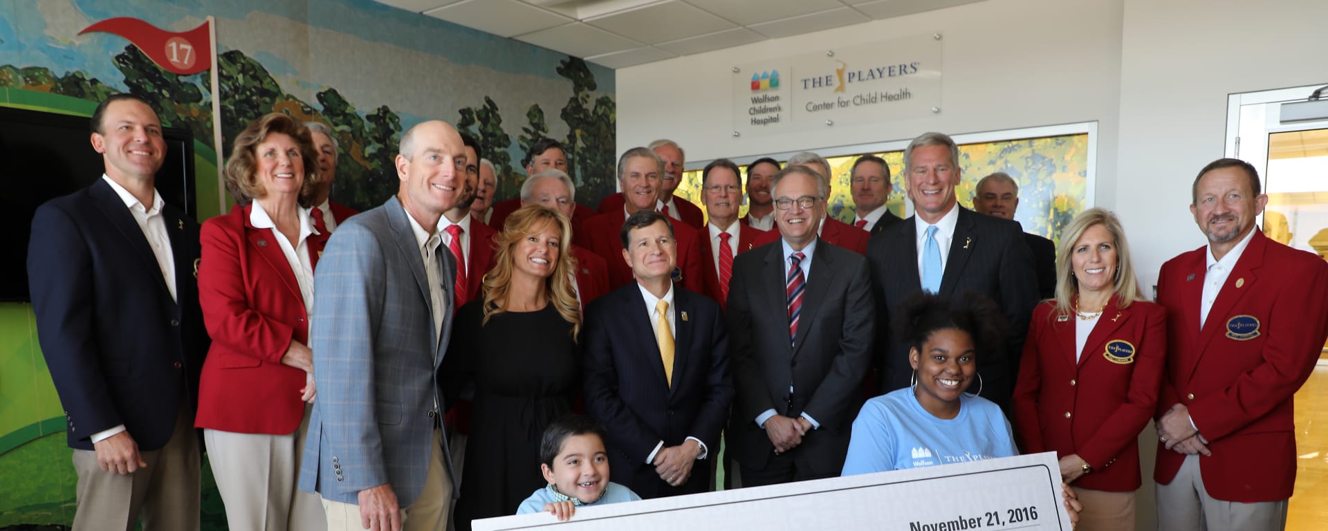 a group of adults from The Players present an oversized check to two Wolfson Children's patients.