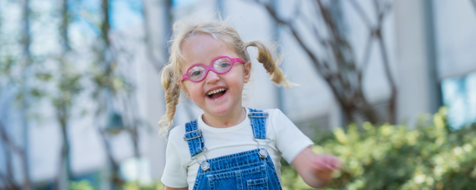 young girl in pink glasses and overalls running outside and smiling