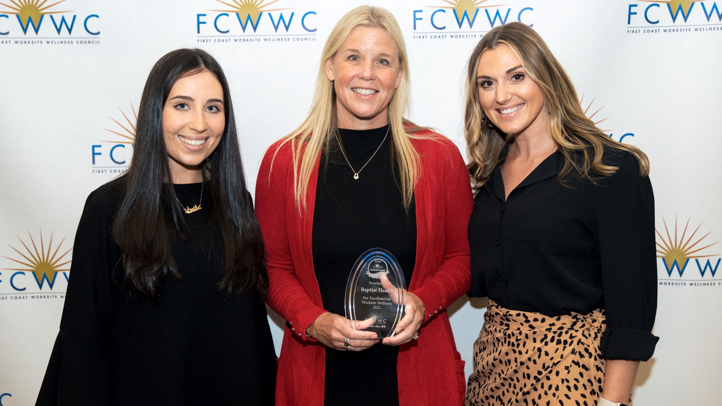 Three women stand together, holding an award
