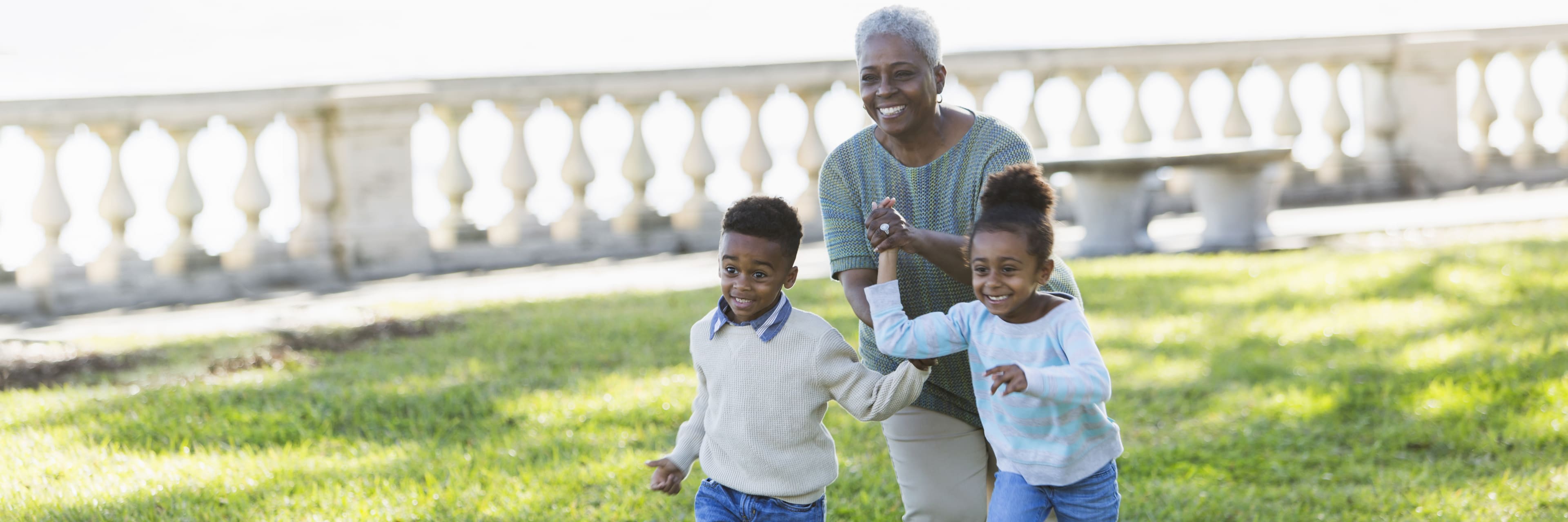 excited children running with their smiling grandmother in the backyard