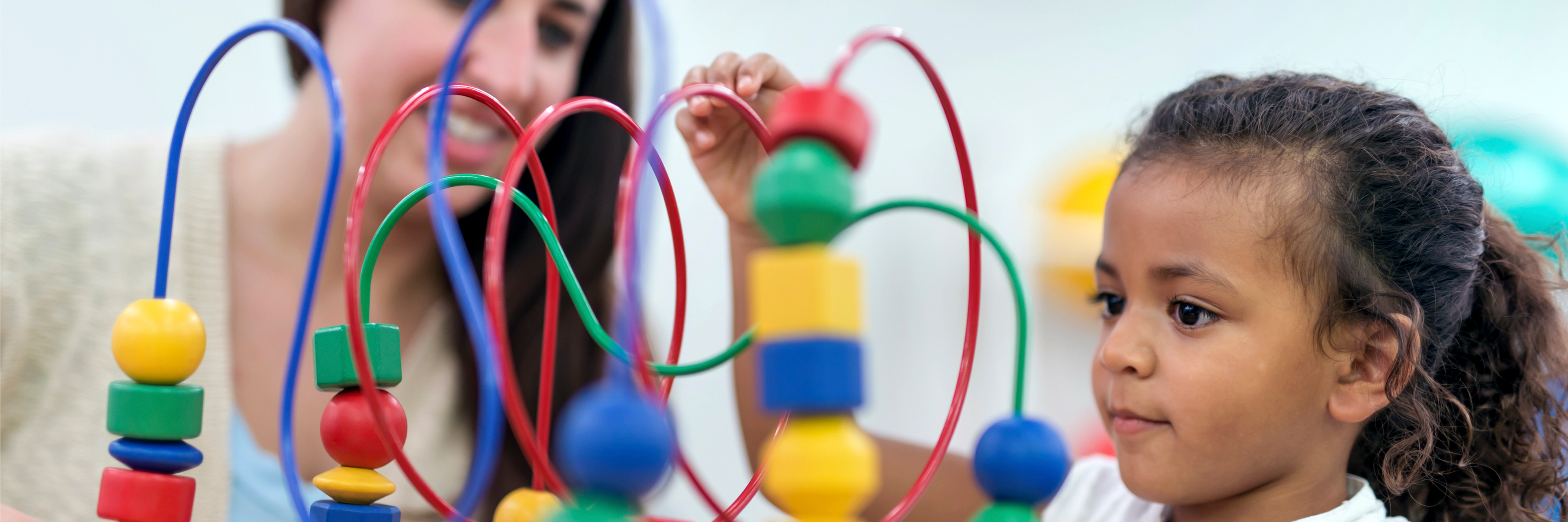 photo of a young girl playing with a colorful block toy as a woman looks on