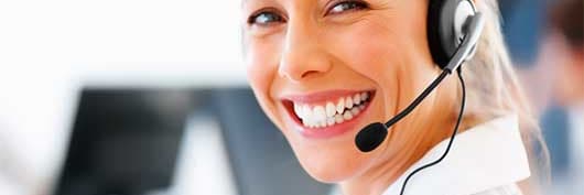 smiling blonde woman wearing a headset with computers in the background
