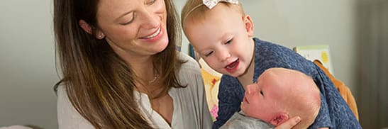 mother and toddler smiling at newborn