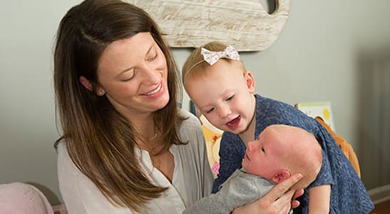 mother and toddler smiling at newborn