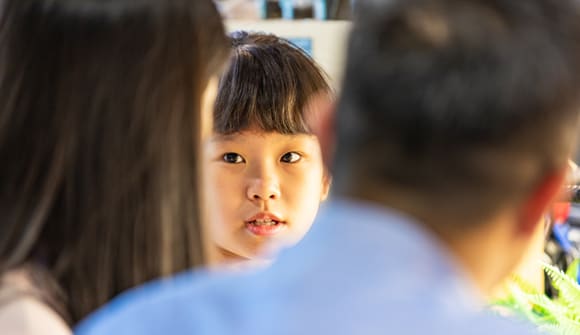 close up of young girls face and the back of her parents' heads