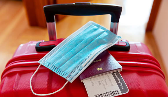 close up of the top of a suitcase with a passport, boarding pass and disposable mask on top