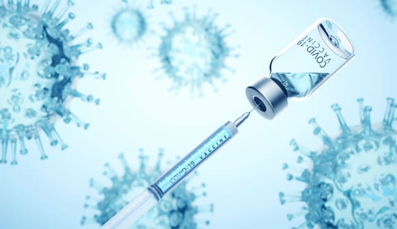 Photograph of a needle entering a bottle filled with fluid. The picture represents a new vaccine, with the needle enterering the glass bottle.