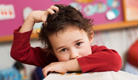 young boy in a red shirt scratching his head