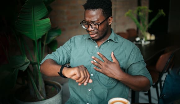 man clutching his chest and looking at his smartwatch
