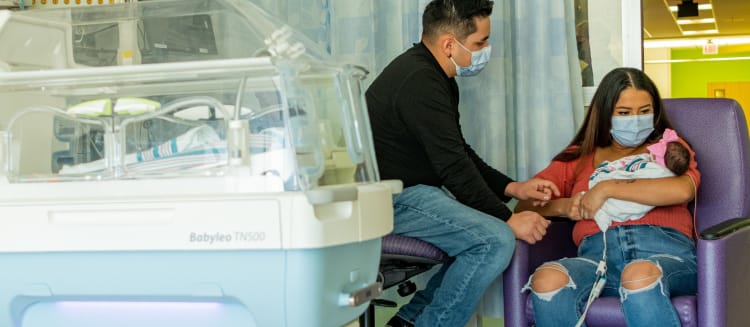 mother holding premie baby in the Wolfson Children's NICU with father looking on.