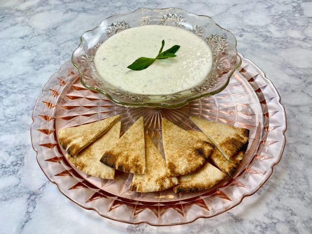 Tzatziki sauce in a crystal bowl with toasted pita triangles on the side