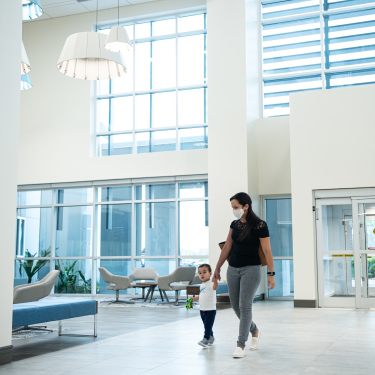 mother and toddler son walking hand in hand in the ligh-filled lobby of HealthPlace at Nocatee