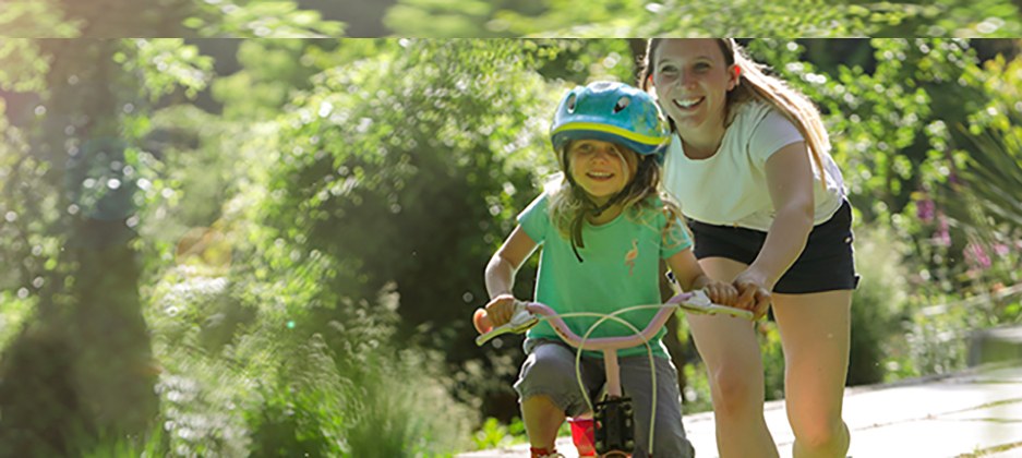 mom teaching her daughter to ride a bike outdoors