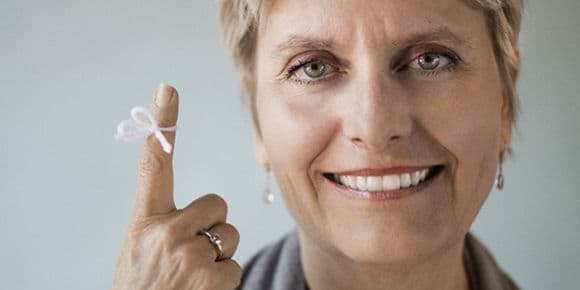 woman smiling with a piece of yarn tied in a bow around her finger