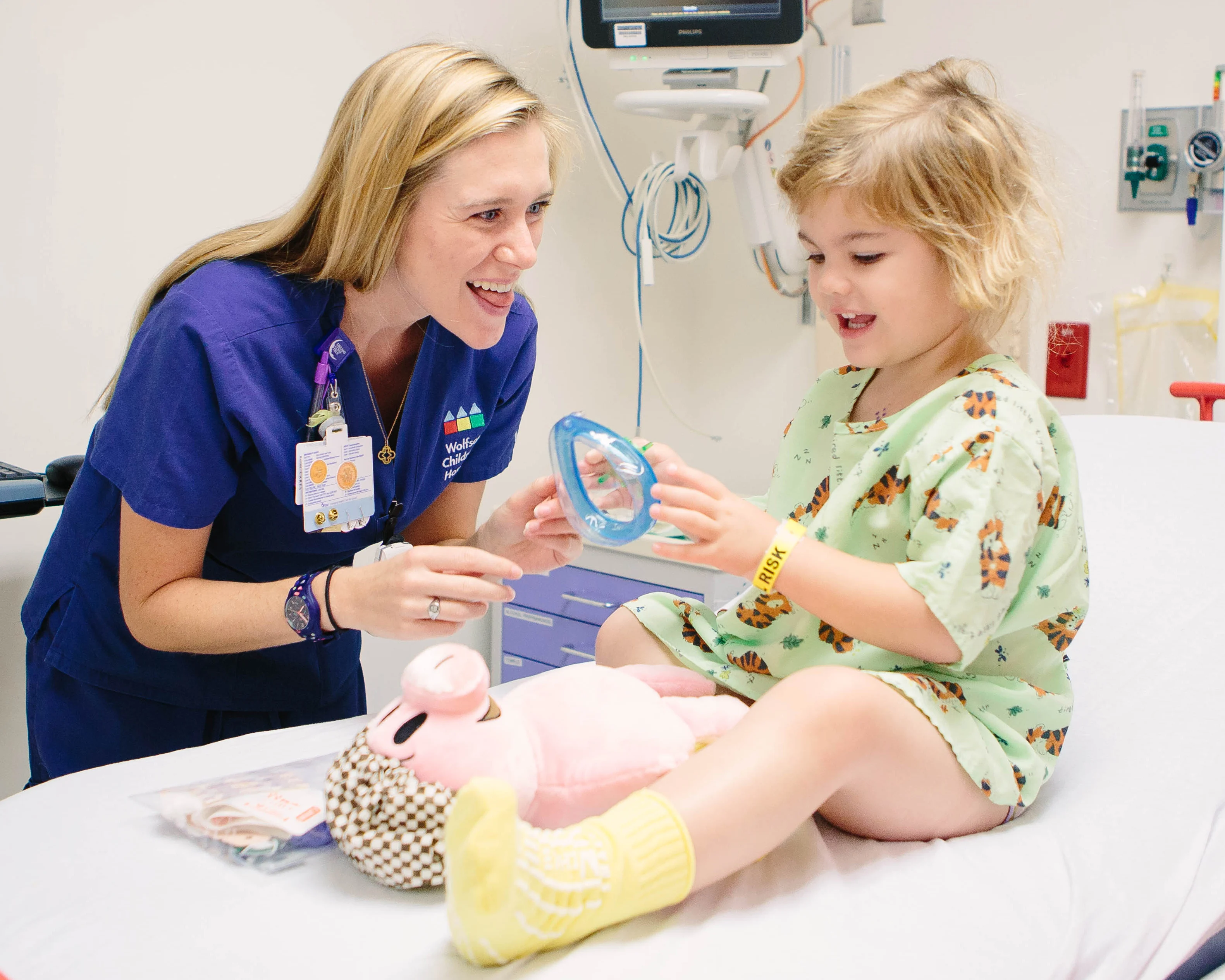child life specialist plays with young girl sitting in a hospital bed