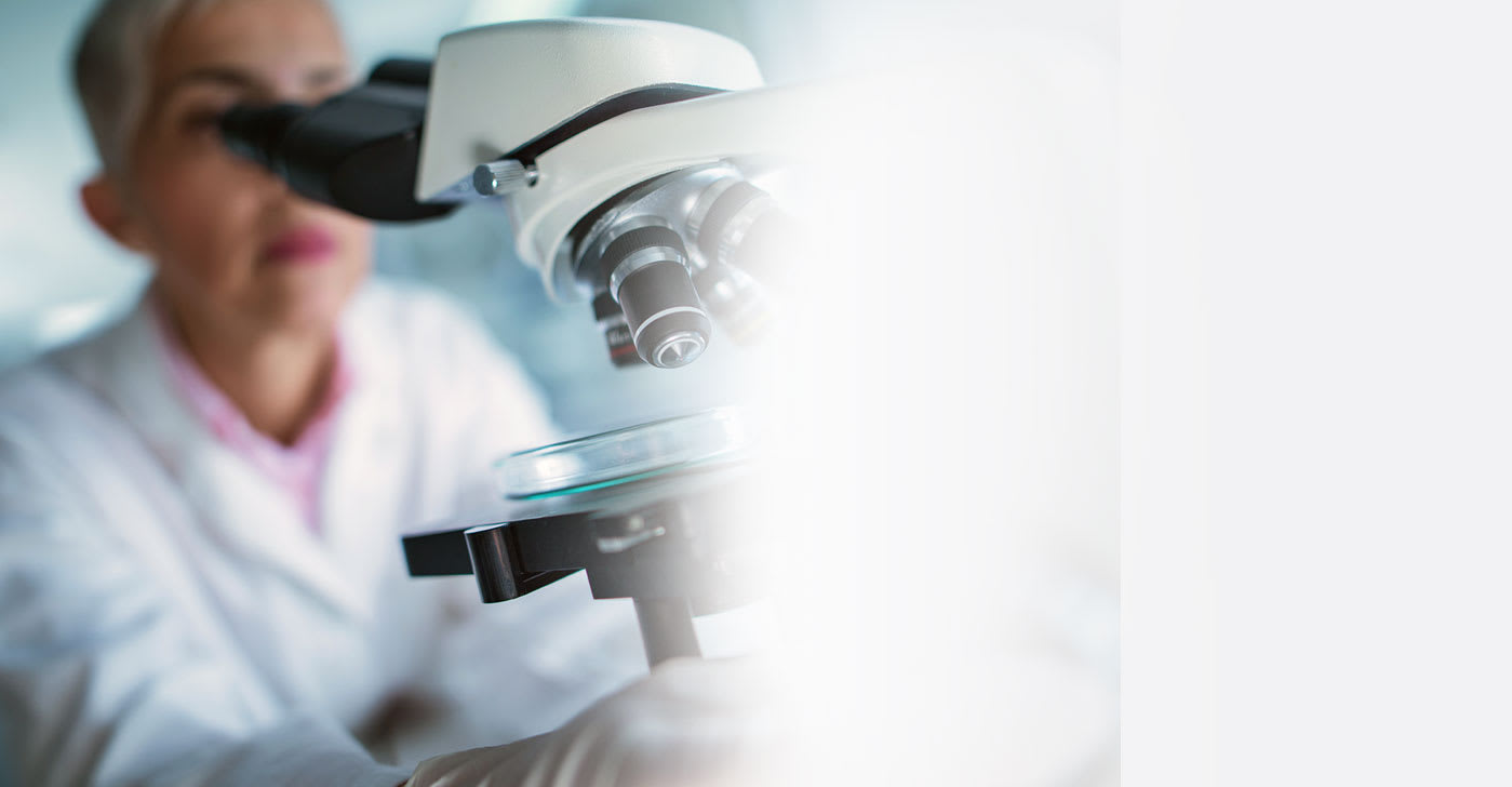 A female clinical trials researcher looks through microscope.