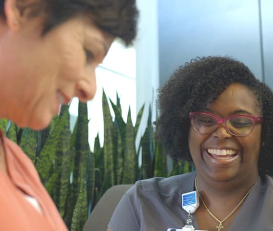 A cropped photo of a smiling nurse navigator sitting with a female patient in the Baptist MD Anderson lobby.