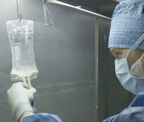 A Baptist MD Anderson oncologist, dressed in medical garb, holds a IV bag of medication.