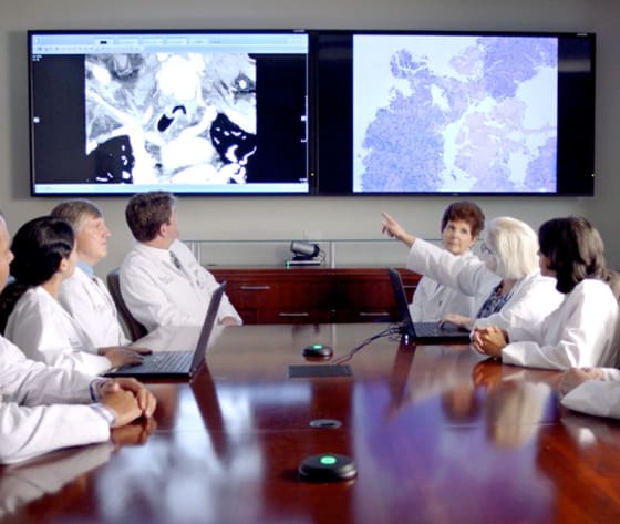 A group of physicians meet for a cancer conference, cancer slides enlarged on mounted flat screens.