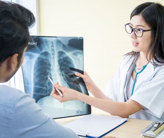 A female healthcare professional uses a pen to point at a lung X-ray.