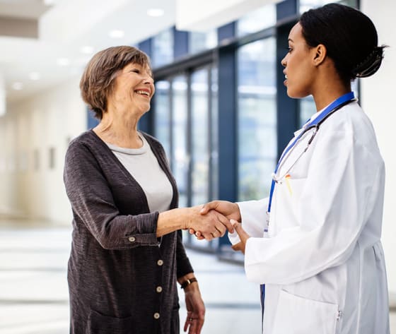 A female physician shakes hands with a female, senior patient wearing a cardigan.