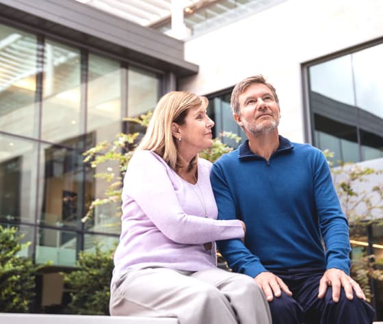 A man sits with his wife in the Baptist MD Anderson courtyard looking up into the sunlight.