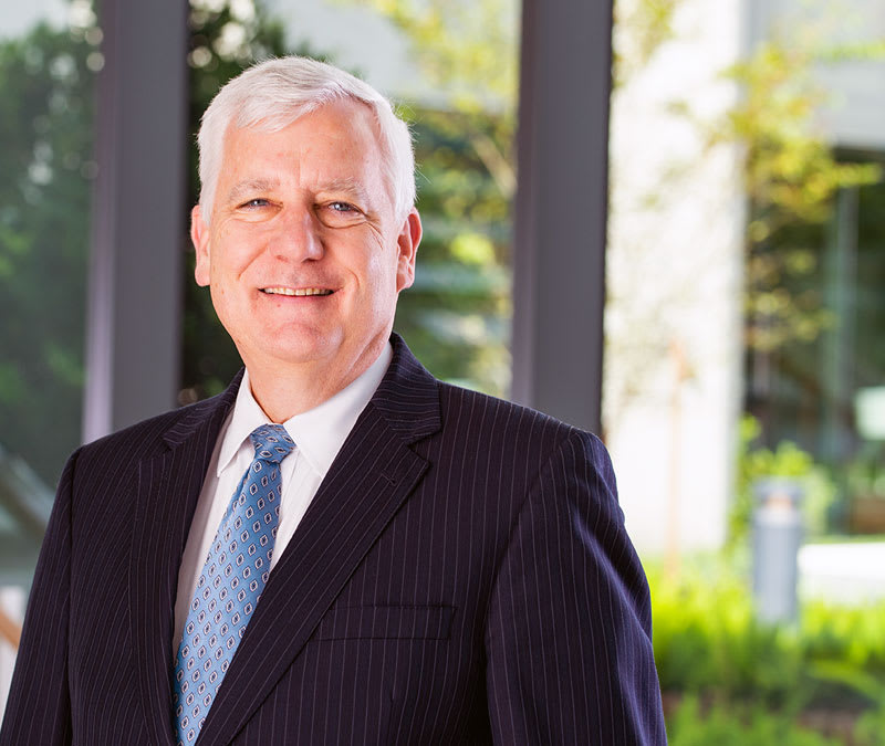 A headshot of a smiling Dr. Putnam in a suit, standing in front of the Baptist MD Anderson courtyard.