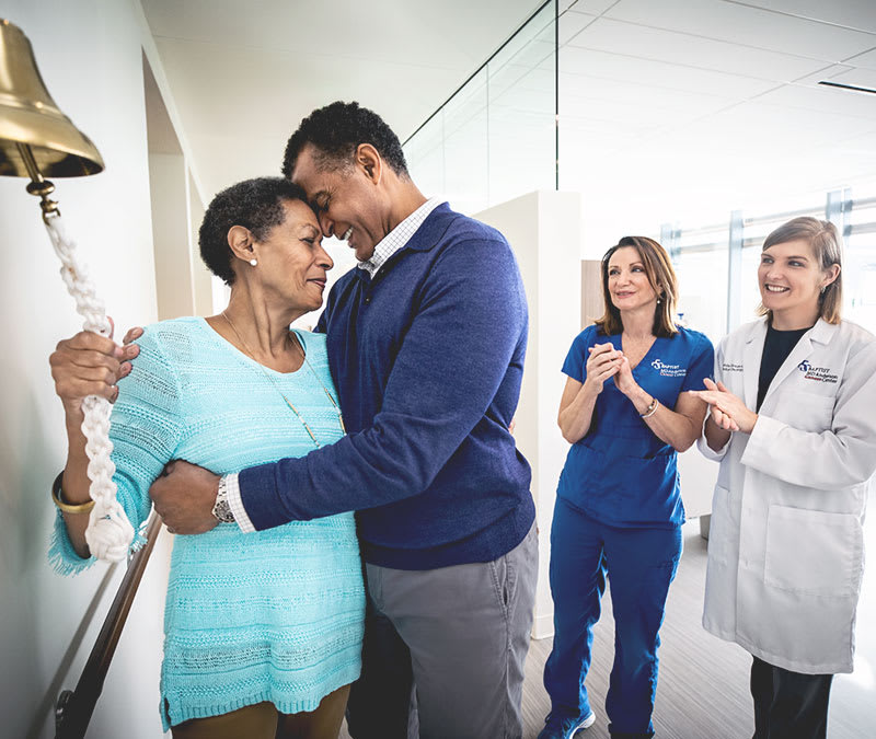 a female patient rings the survivorship bell, her husband by her side, to celebrate the end of treatment.