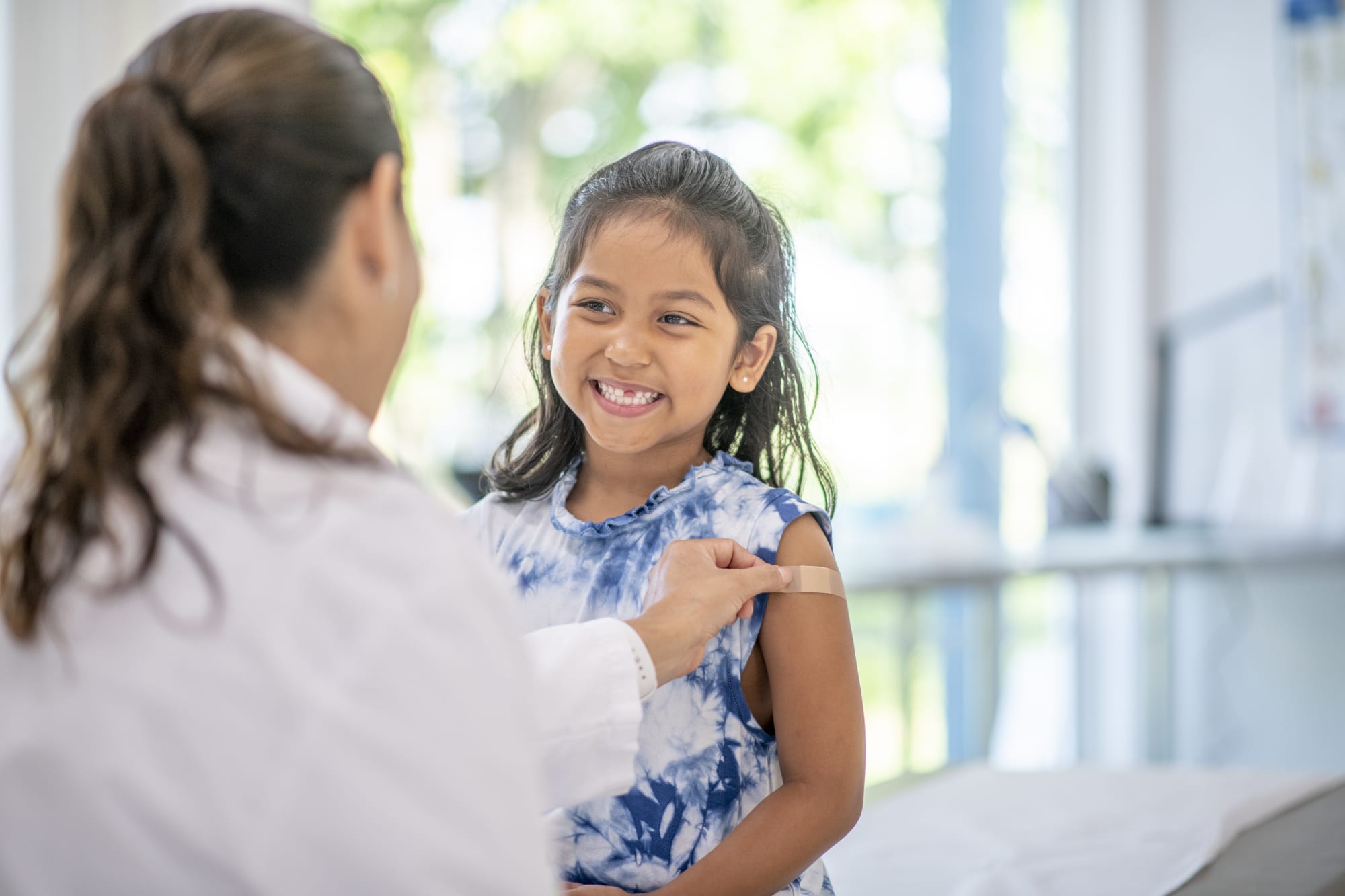 child interacts with the female Hispanic doctor at a medical appointment.