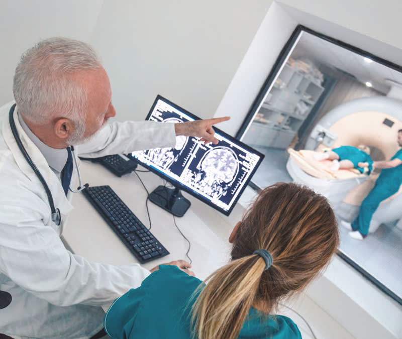 Healthcare professionals examining a patient's brain scan, an MRI machine in the background.