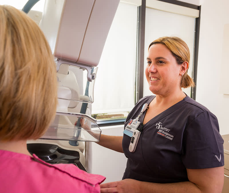 A mammogram technician stands next to the machine and a female patient.