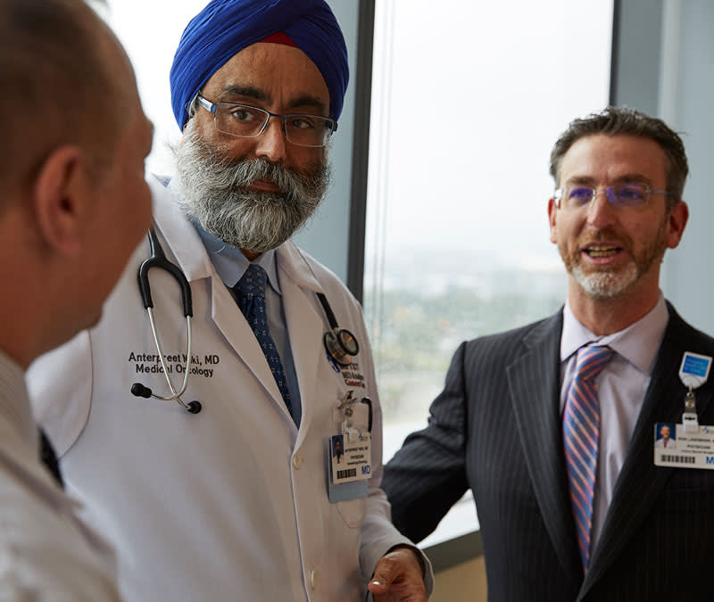 Dr. Neki, Dr. Landman and Dr. Zaiden stand in conversation in front of a beautiful view of the river.