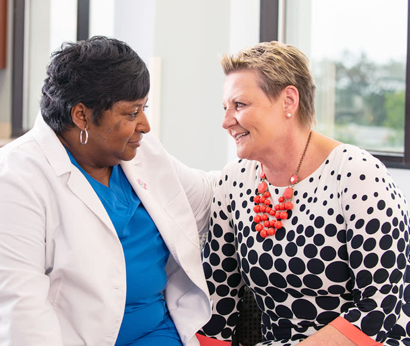 A female nurse smiles with her arm around a smiling patient and survivor.