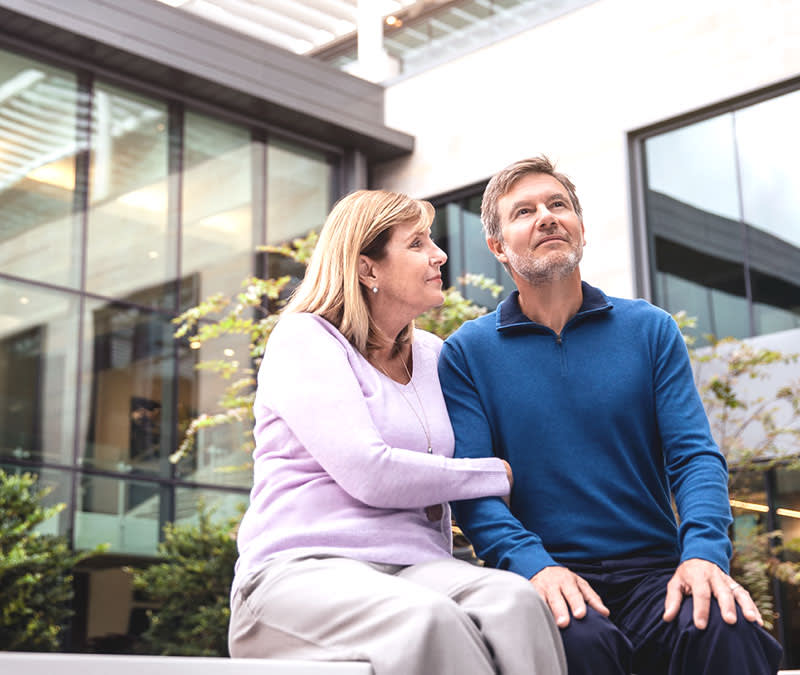 A man sits with his wife in the Baptist MD Anderson courtyard looking up into the sunlight.