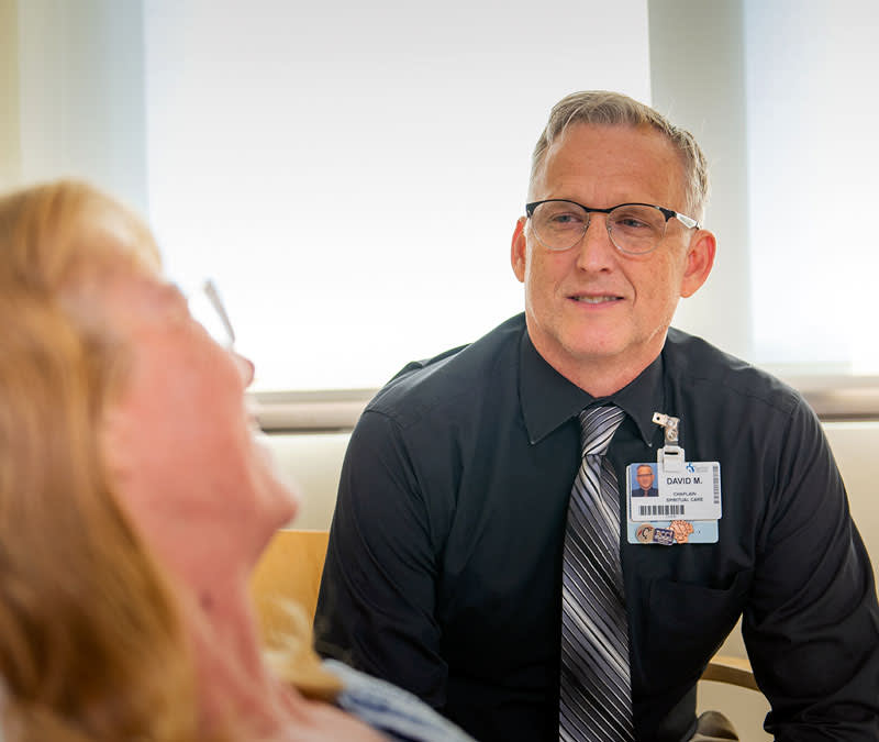 A male chaplain sits, listening to a female patient.