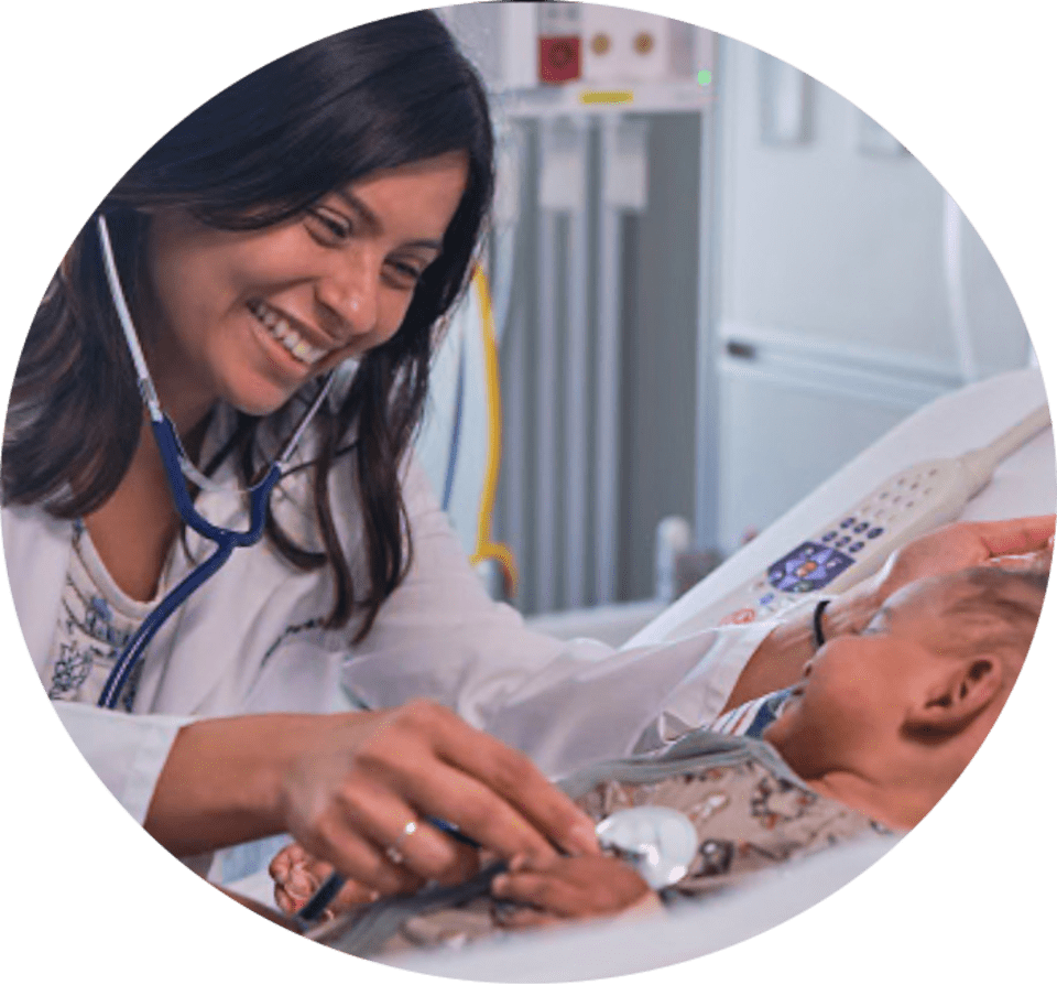 female physician smiling at a baby in a hospital bed while placing a stethoscope on its chest.