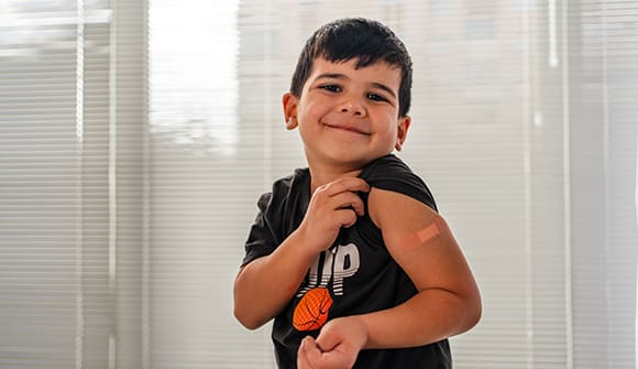 young boy showing his bandaged shoulder after getting a shot