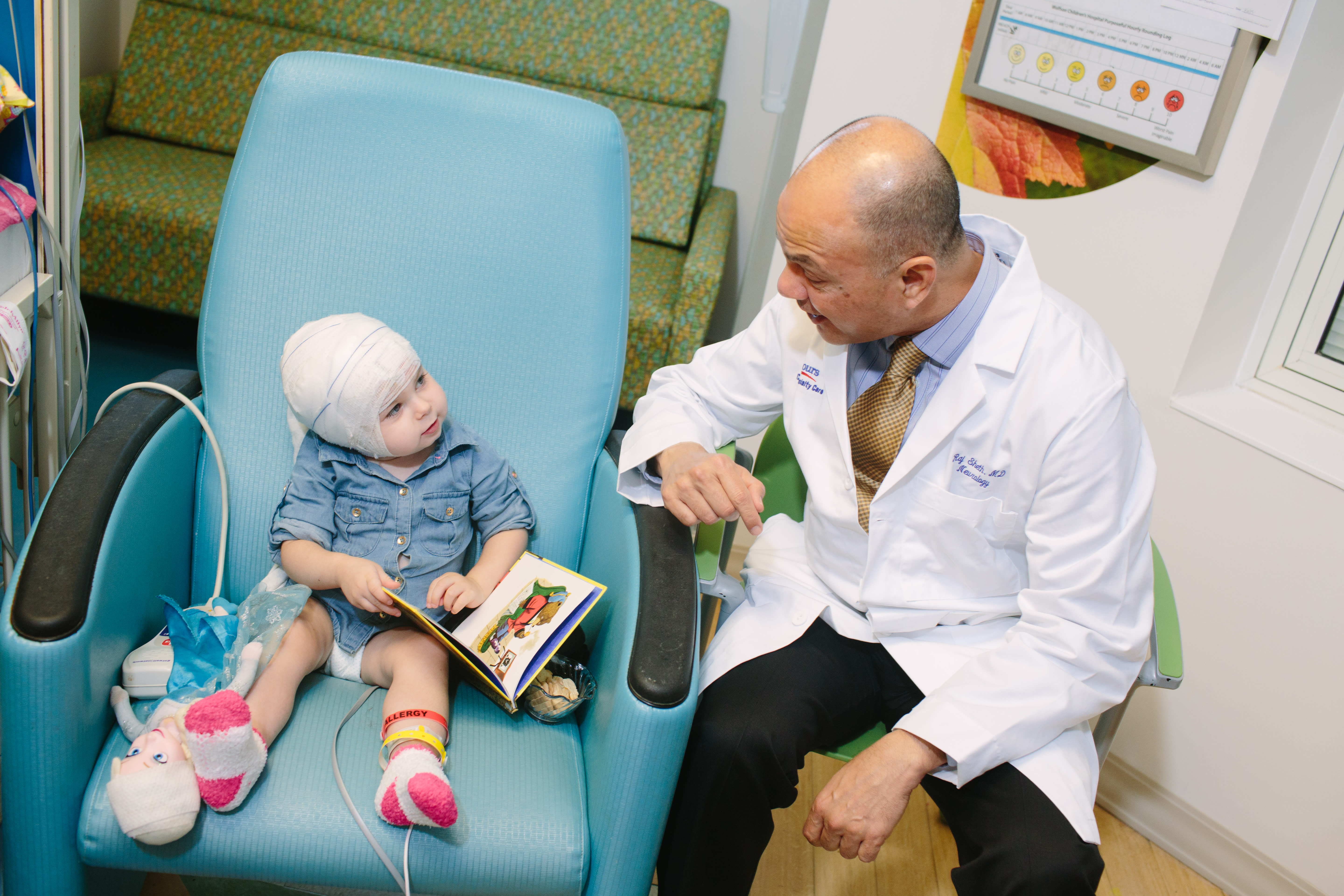 Pediatric epilepsy patient sitting in chair looking at book with doctor beside her