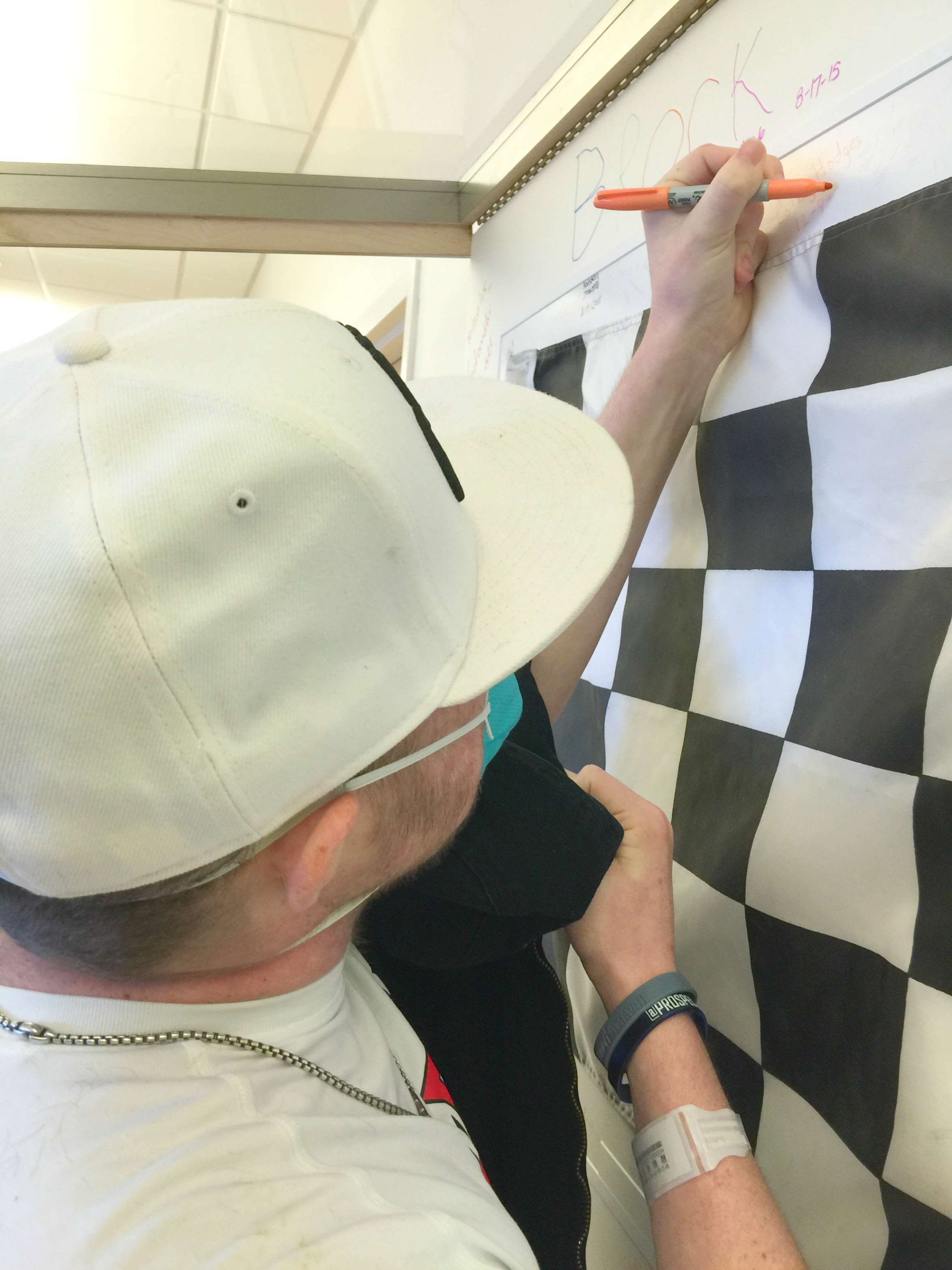 A pediatric cancer patient signs and dates the checkered flag